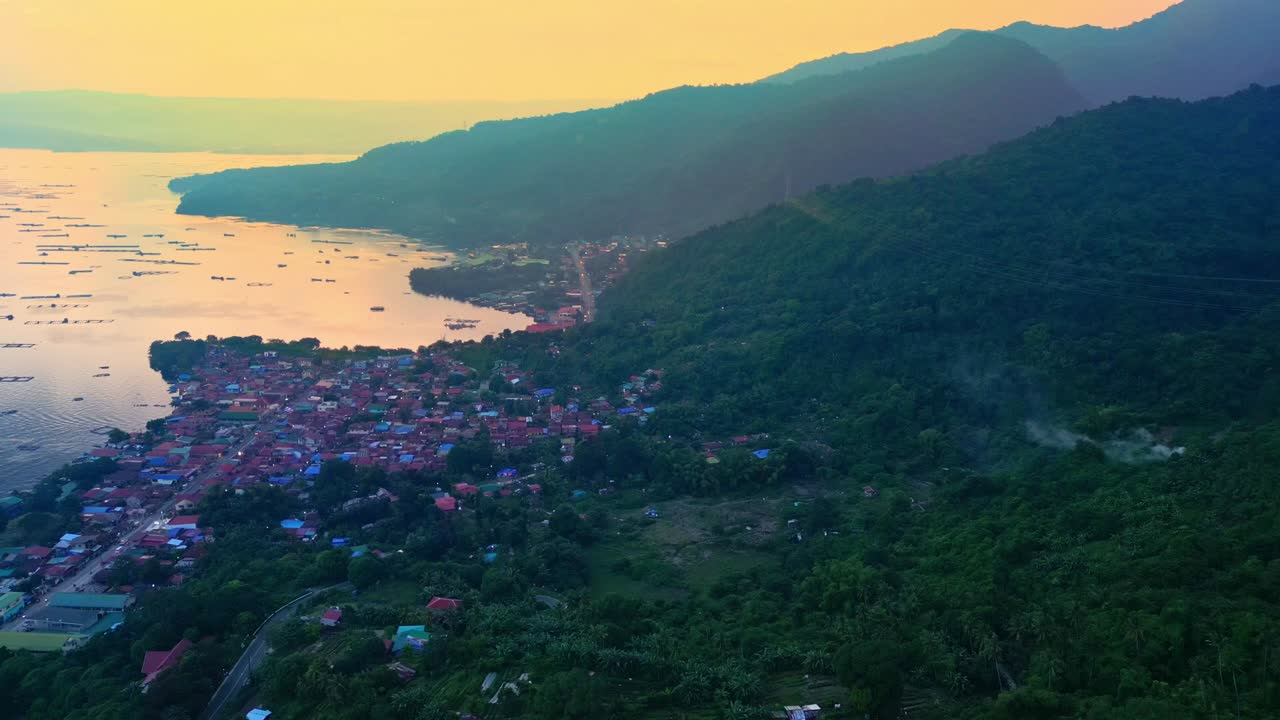 A descending aerial of golden sunset over Talisay and Taal Lake fading into winding forest road in Batangas, Philippines