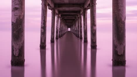 a tranquil view under a coastal pier, bathed in soft pink hues, showcasing serenity and the beauty of nature's reflections on calm waters