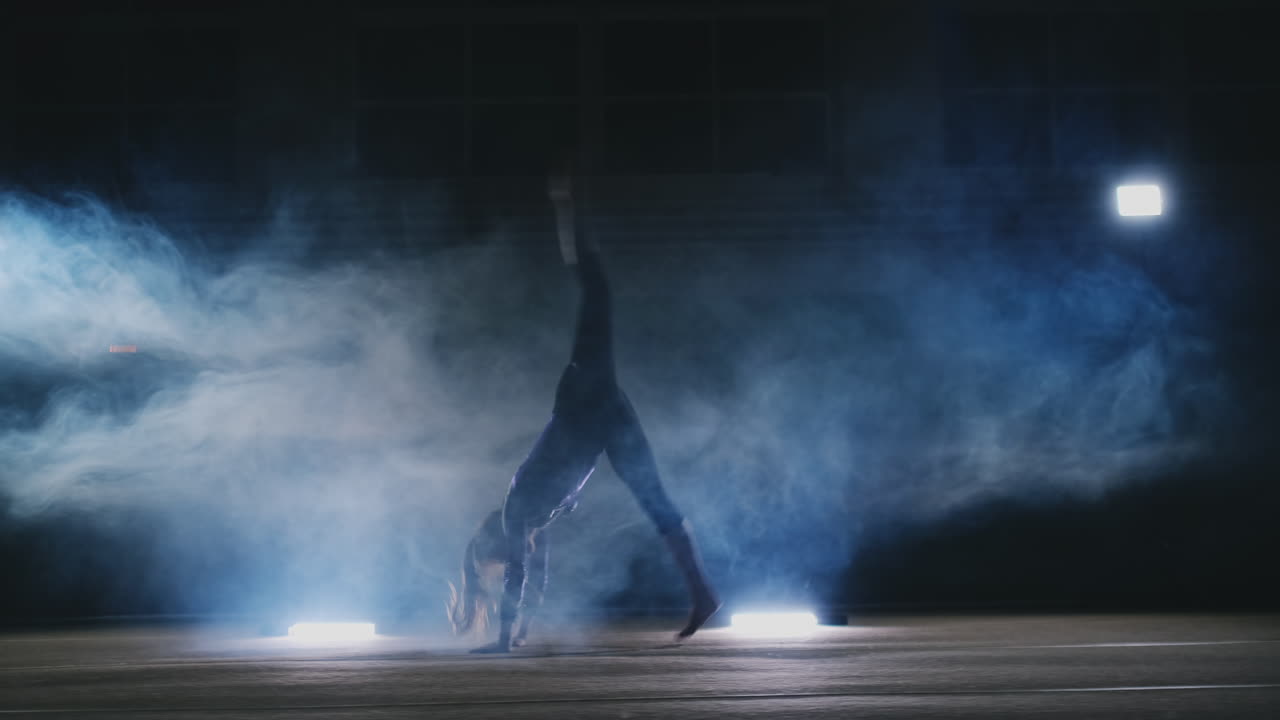 In slow motion in the smoke girl acrobat performs several back flips and coups in the air.