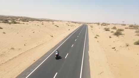 aerial drone shot of a bike rider navigating curves on a remote desert road surrounded by sand.