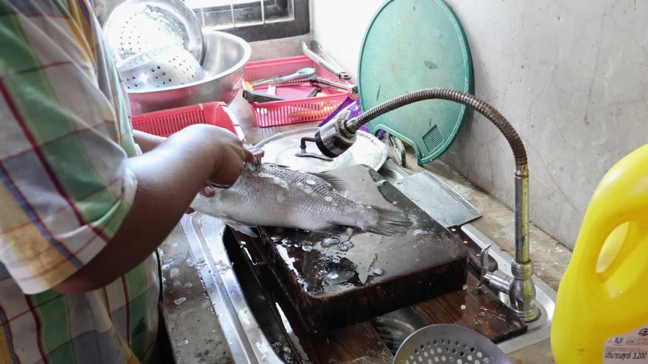 persona descascando peces con agua corriente.