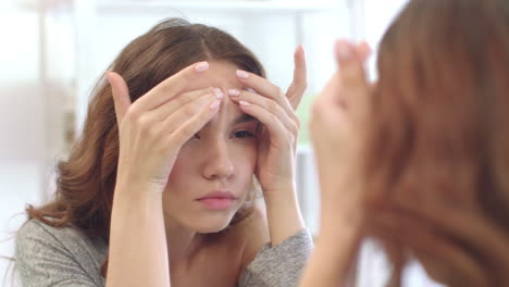 Young-teenager-girl-squeezing-acnes-on-skin-face-front-mirror-in-bath-room