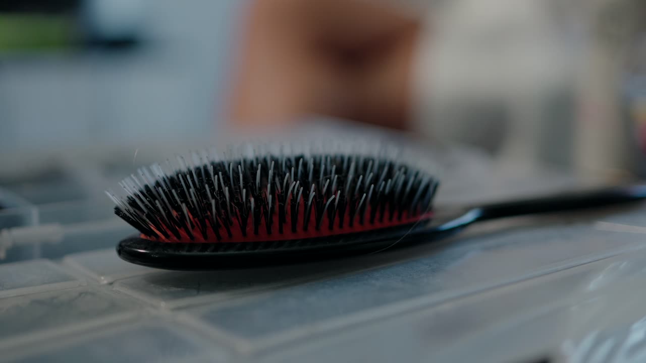Nærbillede af en sort og rød hårbørste, der hviler på et plastikbord indendørs.