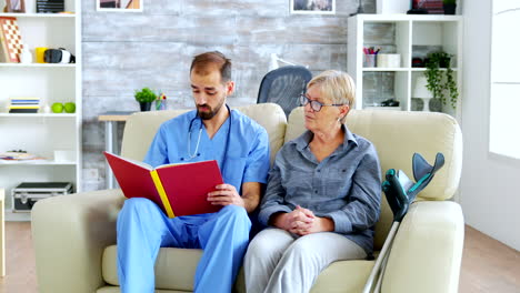 asistente masculino en un hogar de ancianos leyendo un libro a un jubilado anciano