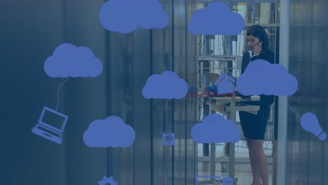 Animation-of-clouds-icons-over-biracial-female-worker-inspecting-server-room