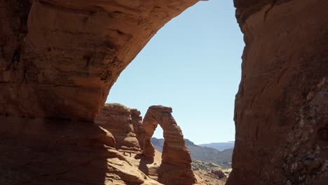 tilt up extreme wide shot of a beautiful natural red sandstone rock arch from a natural rock window