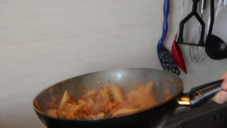 man cooking pasta in his home, mixing pasta in the pan