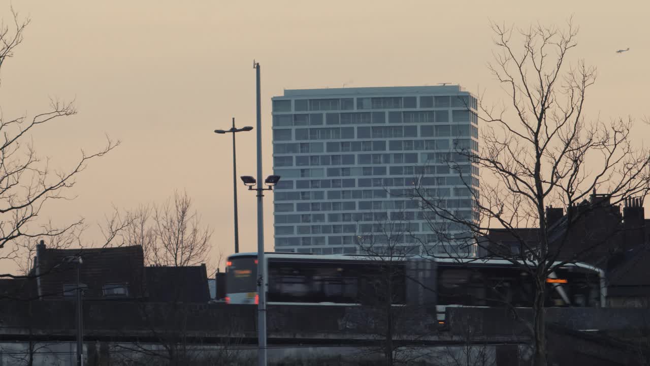 A city bus crosses an aging flyover with historic low-rise buildings in the foreground and the modern Antwerp Tower in the background, highlighting urban contrast