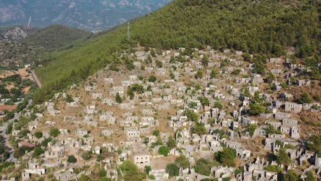 drone aéreo volando hacia atrás sobre casas abandonadas y ruinas de un pueblo griego en una montaña llamada kayakoy en fethiye turquía durante un día de verano