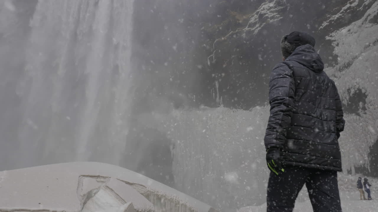 따뜻한 옷을 입은 남자의 등 아이슬란드의 추운 겨울 풍경에서 폭포  ⁇ 에 눈을  ⁇ 고  ⁇ 고