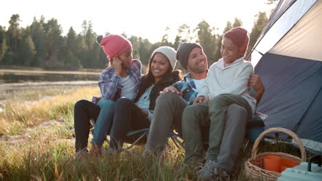 Parents-and-two-children-sit-talking-outside-tent