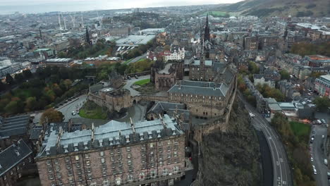 Sweeping-drone-shot-of-Edinburgh-castle-at-sunrise,-revealing-the-impressive-grounds-from-above-and-moving-slowly-away