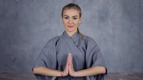 Smiling-female-coach-yoga-in-robe-makes-Namaste-gesture-by-hands