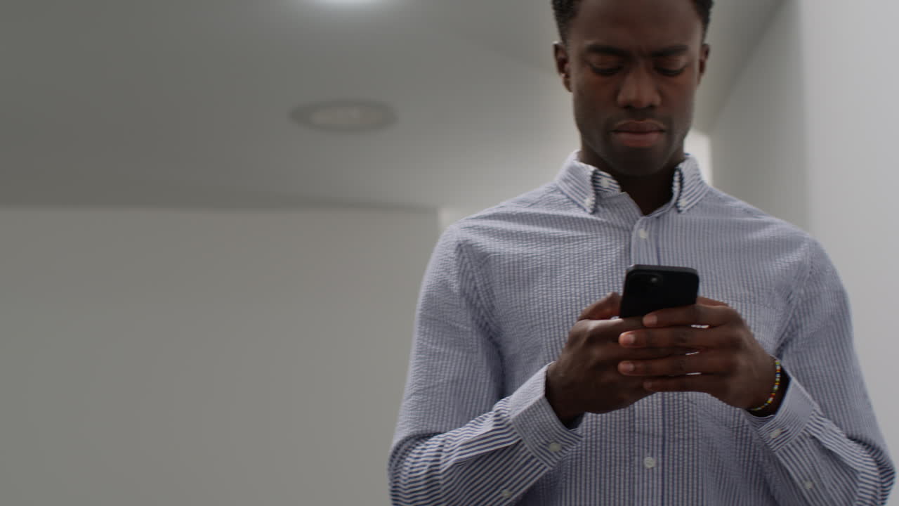 Young Businessman In Office Looking At Message With Bad News On Mobile Phone And Leans Against Wall Looking Unhappy And Depressed 2