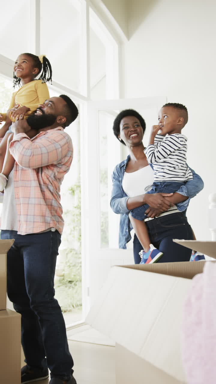 Vertical video of happy african american parents holding son and daughter at home, slow motion