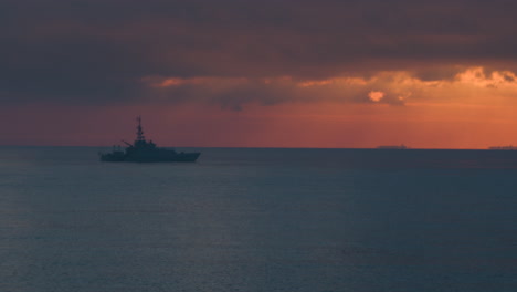 wide aerial view of a royal navy warship sailing on a calm sea at sunrise