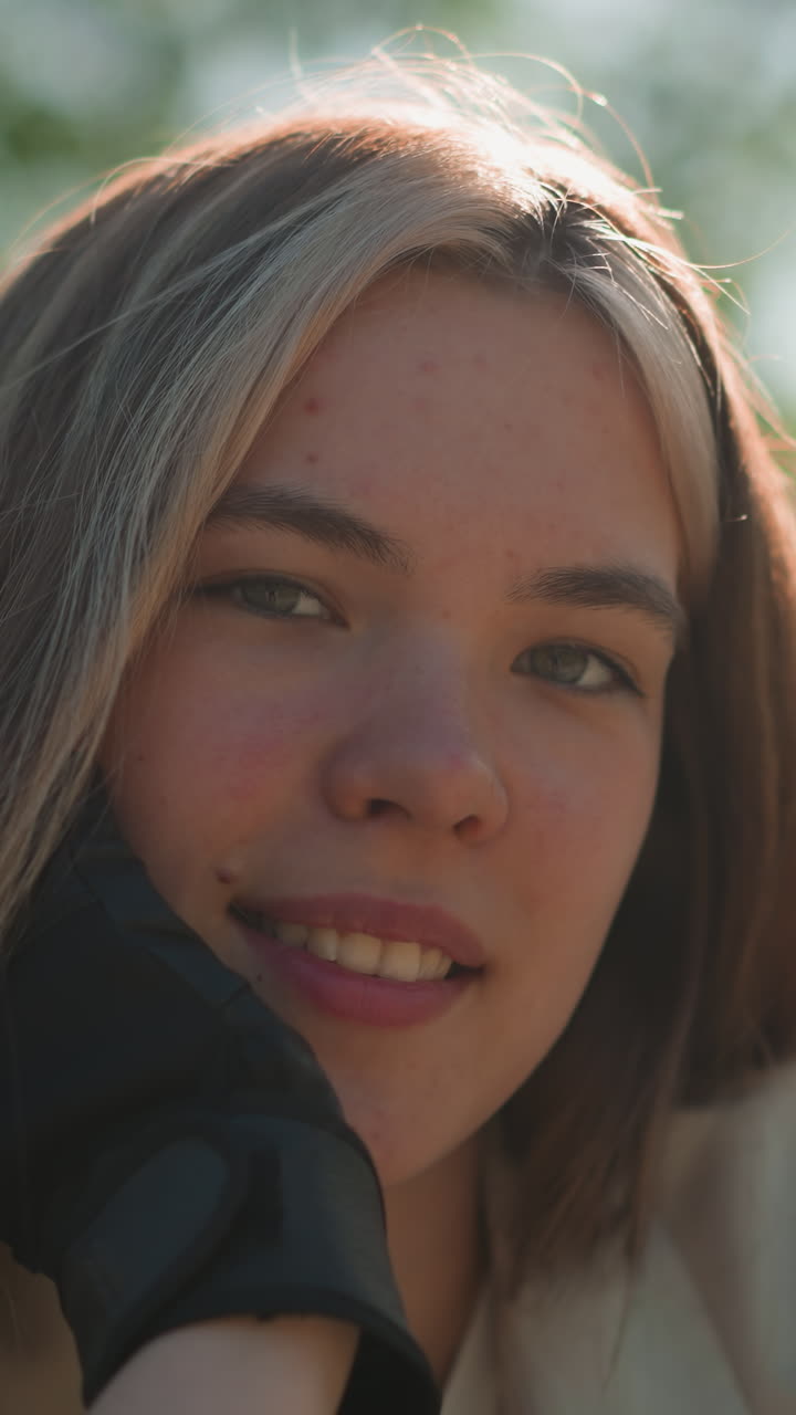 primer plano de una mujer joven apoyada en el manillar de la bicicleta, la mano apoyada en la barbilla con una sonrisa suave y contemplativa, la luz del sol ilumina suavemente su rostro contra un fondo borroso de frondoso follaje verde