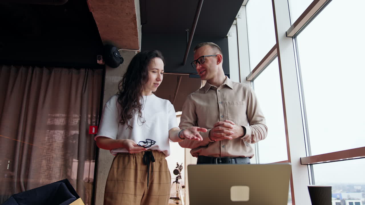 Office employees discussing the project on the laptop. Young people talk pointing at the screen, looking for the problem solutions. Low angle view.