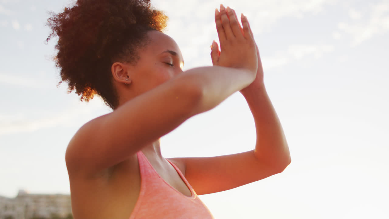 Donna afroamericana che pratica yoga e medita sulle rocce vicino al mare