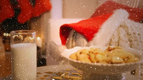 video composition with falling snow over desk with cookies, santa hat, and milk glass