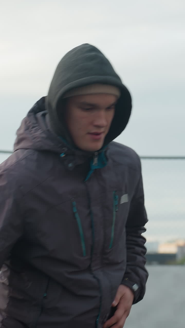 hombre enfocado en sudadera hábilmente controlando la pelota de fútbol con trabajo de pies preciso en la arena deportiva, el fondo urbano presenta una barrera amarilla, valla y edificios residenciales distantes