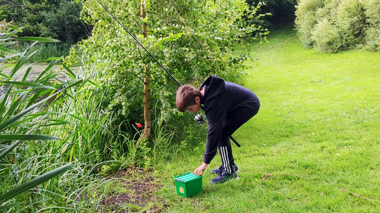 4k 60fps niño está poniendo nuevo cebo en el gancho de pesca mientras pesca en un estanque en dinamarca - tiro constante de mano