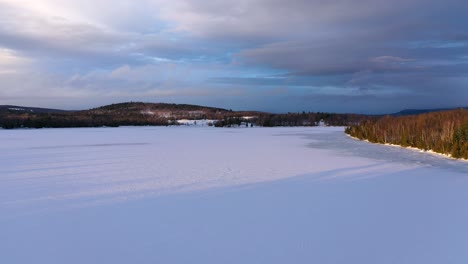 Aerial-slide-high-above-frozen-lake-at-sunset-with-dark-moody-skies-and-golden-light