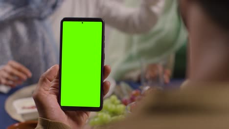 man looking at green screen mobile phone sitting around muslim muslim family table at home eating meal