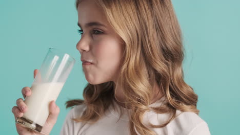 teenage caucasian girl in pijamas drinking milk from a glass and smiling.