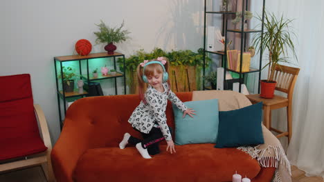 niña feliz niña con auriculares bailando y saltando mientras escucha la música en casa sola