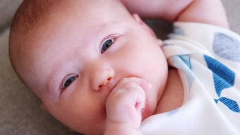 Slow-Motion-Close-Up-Shot-Of-Newborn-Baby-Boy-Lying-With-Hand-In-Mouth-On-Sofa-At-Home