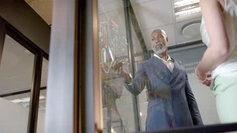 african american businessman writing on glass wall in office with copy space