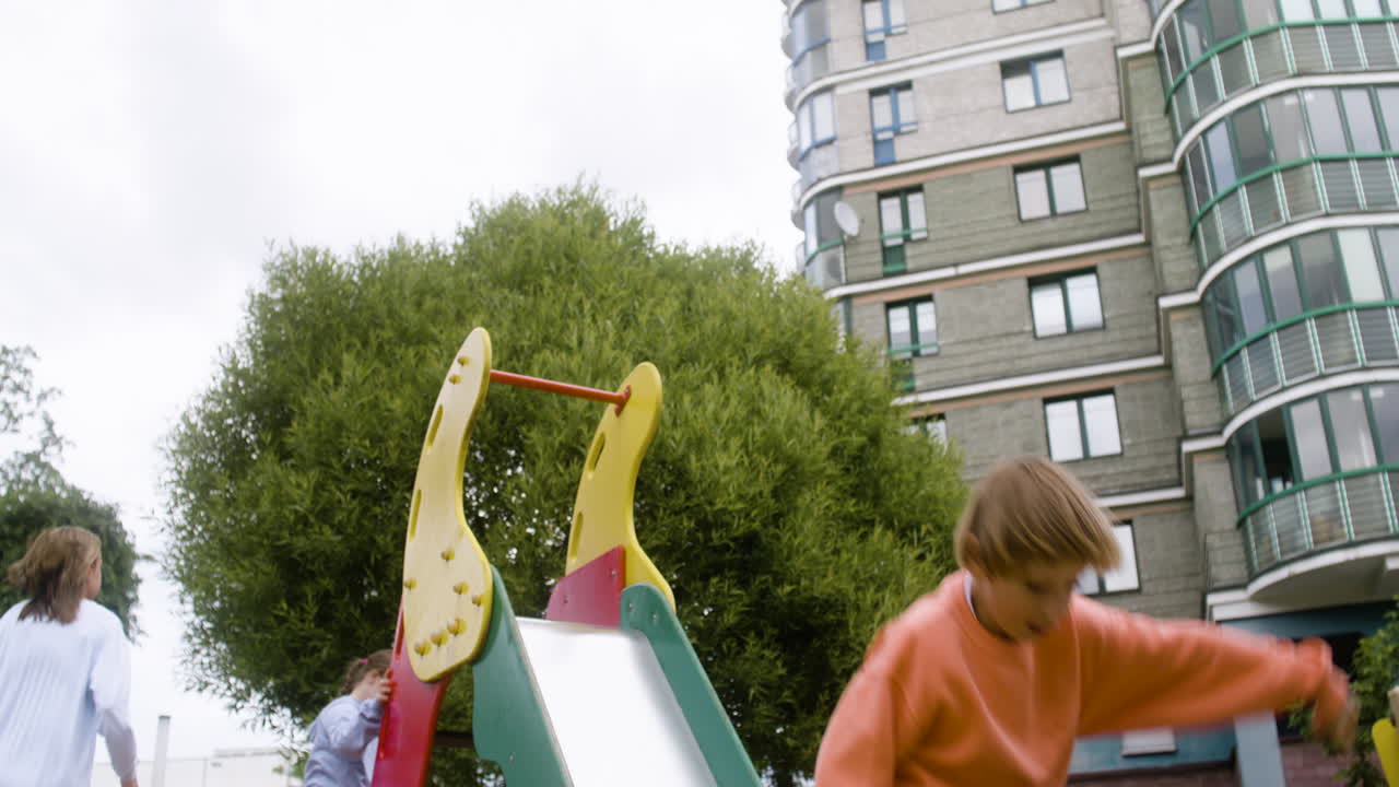 바람이 불는 날 공원에서 다른 아이들과 함께 놀고 있는 다운 증후군을 가진 작은 소녀의 아래 시야. 그들은 슬라이드에 올라가고 있습니다.