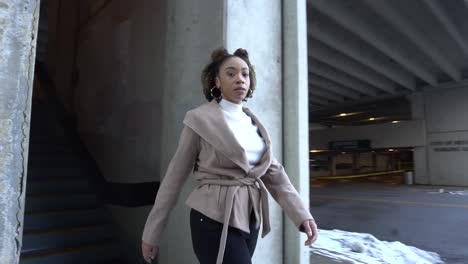 black model walks from parking garage into an alley, showcasing her attire