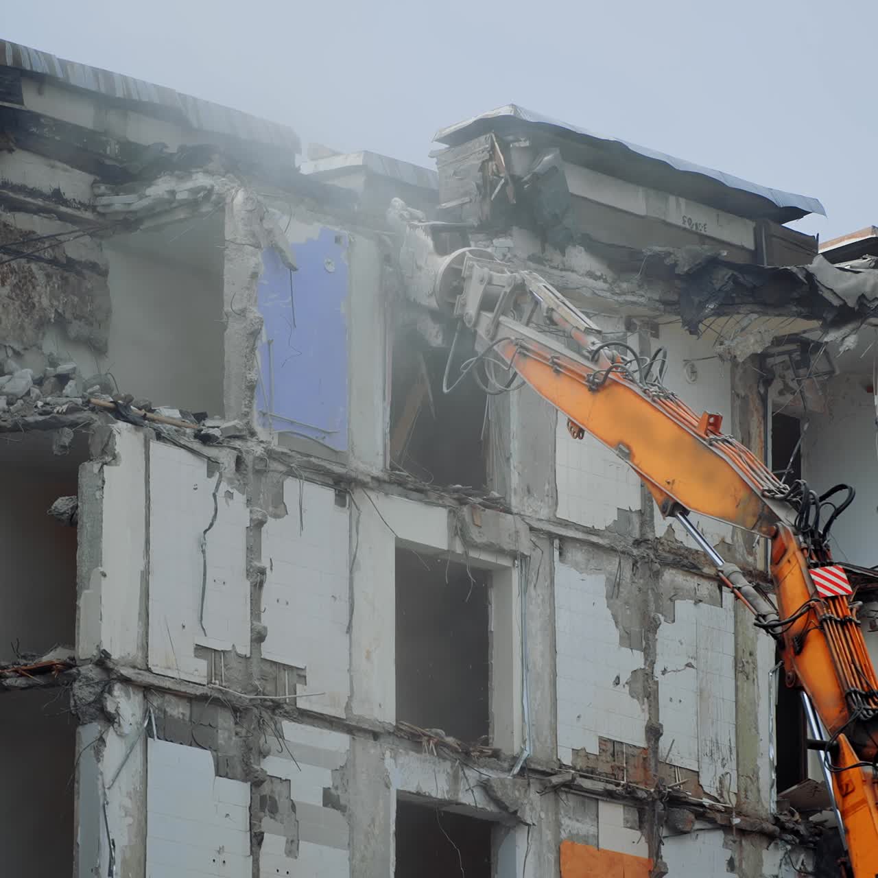 Excavator long claw working in a dusty cloud. Demolishing machinery destroys the roof of an old house. Debris falling heavily from the roof