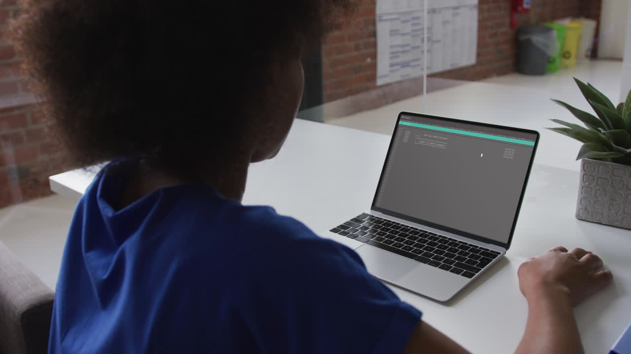 African american woman sitting at desk watching coding data processing on laptop screen