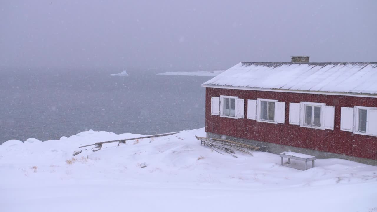 카누와 빙산이 있는 눈보라 속에서 북극 해안에 있는 빨간 보트 하우스의 슬로우 모션 비디오