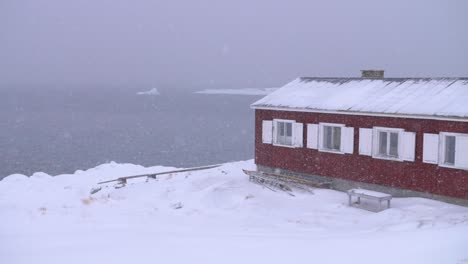 Video-En-Cámara-Lenta-De-Una-Casa-De-Botes-Rojos-En-La-Costa-ártica-En-Una-Ventisca-Con-Canoas-E-Icebergs