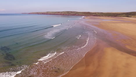 aerial shot looking across the sandy beach at freshwater west in wales, with small waves and sunny skies, while panning right