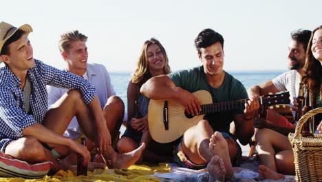 hombre tocando la guitarra para amigos sentado en la playa 4k