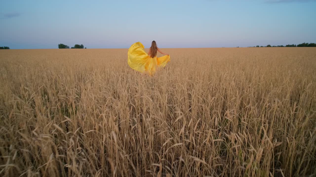 Woman in Yellow Dress Walking Through a Wheat Field at Sunset
