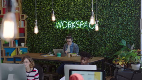 young caucasian man student using laptop computer typing email working eating food in office listening to music wearing headphones