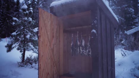 a man inspects deer meat as it smokes within the confines of a smokehouse in indre fosen, trondelag county, norway - close up