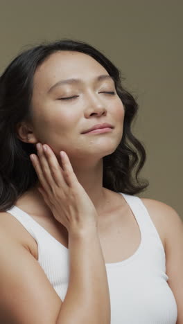 vertical video of asian woman with dark hair touching her neck on beige background, slow motion
