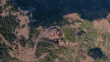 Overhead-flyover-of-road-winding-on-dry-mountain-range-with-trees