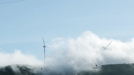 white clouds rolling on lush mountains with wind turbines during hazy morning in serra de aire e candeeiros, leiria portugal