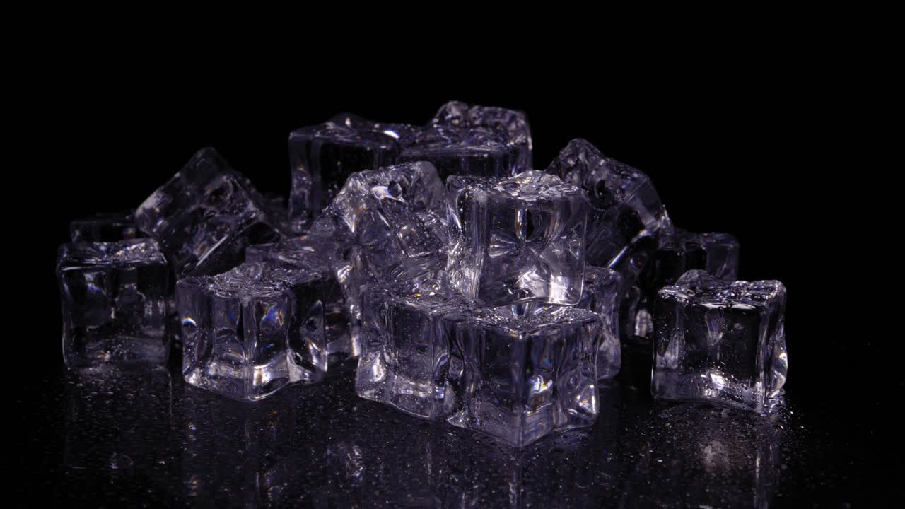 montón de cubitos de hielo con un tinte púrpura girando sobre un fondo negro, disparo de estudio estático hacia abajo