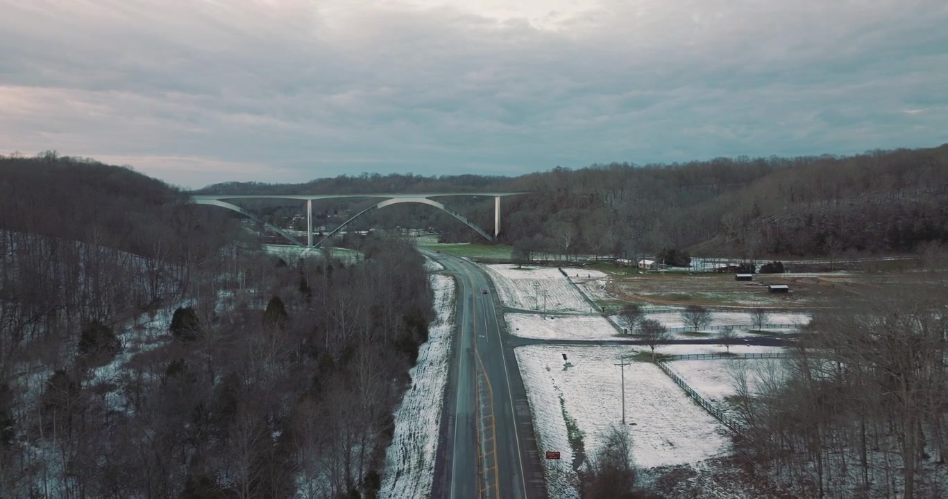 Due auto percorrono un'autostrada innevata al tramonto in direzione del Ponte Natchez Trace a Franklin, Tennessee, con ripresa aerea che le segue.