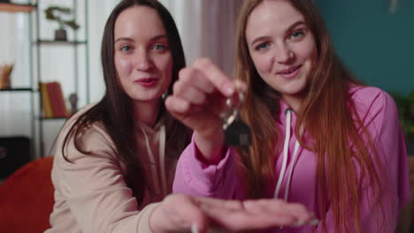 Girls-siblings-homeowners-hugging-and-showing-new-home-apartment-keys,-receiving-mortgage-loan