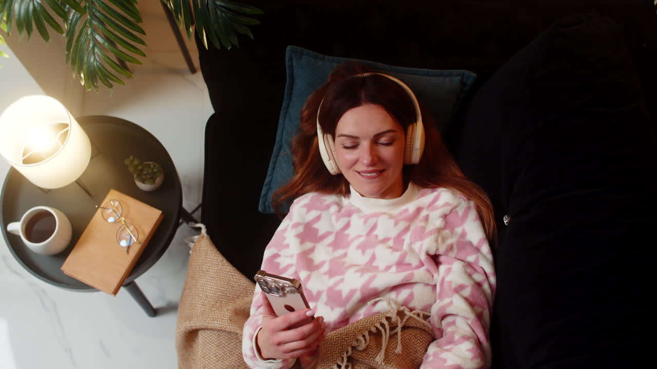 Donna adulta con cuffie wireless che ascolta musica sul smartphone, occhi chiusi, annuisce, sorride e si rilassa